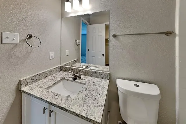 a bathroom with a granite countertop sink a toilet and a mirror