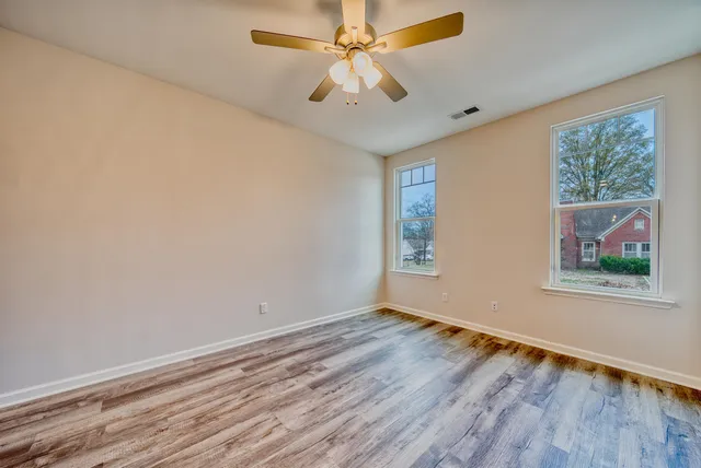 an empty room with wooden floor chandelier fan and windows