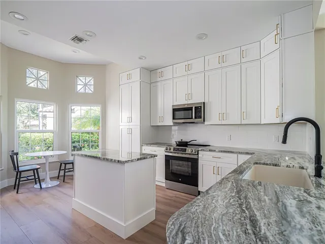 a kitchen with stainless steel appliances granite countertop a refrigerator a stove top oven a sink dishwasher and white cabinets with wooden floor
