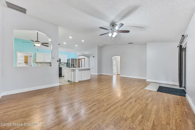 a view of an empty room with wooden floor and a ceiling fan