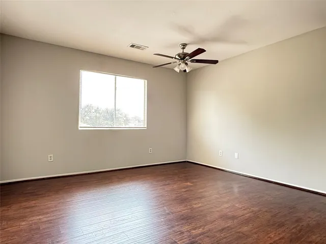 an empty room with wooden floor fan and windows