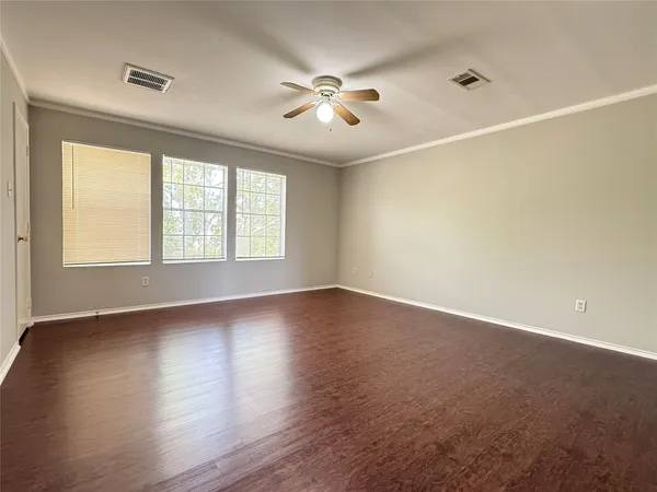 an empty room with wooden floor windows and fan