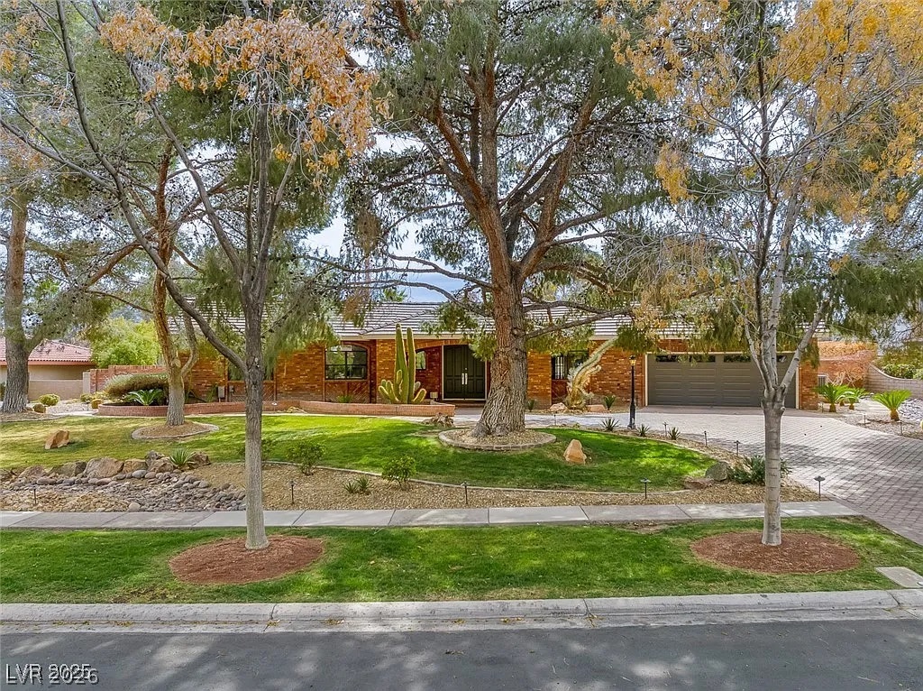 9 Quail Run Road Henderson, NV 89014 - Photo 4 of 57 Mature trees and desert-inspired landscaping frame this charming brick facade with an integrated garage.
