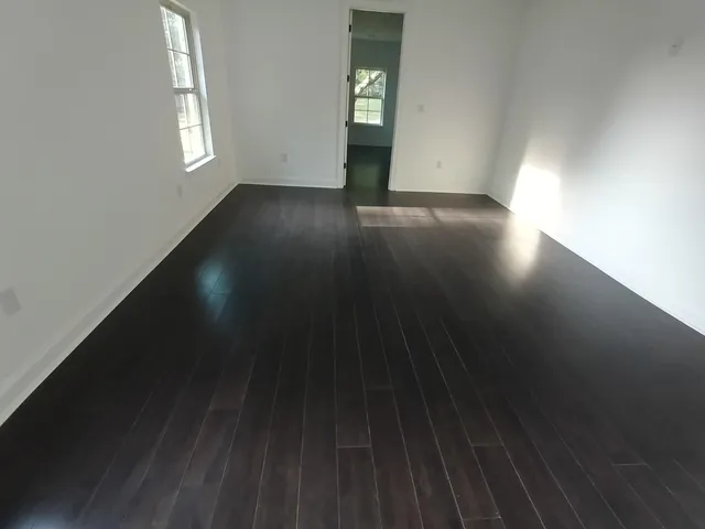 an empty room with wooden floor fan and windows
