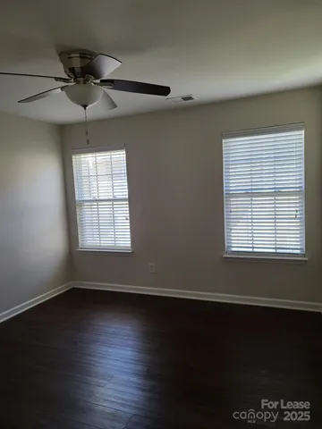 an empty room with wooden floor chandelier fan and windows