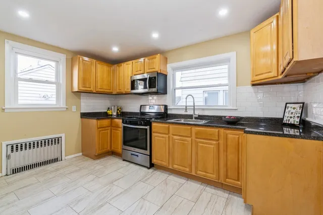 a kitchen with stainless steel appliances granite countertop a sink a stove a refrigerator cabinets and a window