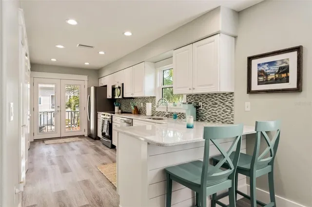 a kitchen with stainless steel appliances granite countertop a stove top oven a refrigerator a sink and a dining table with white cabinets