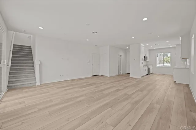 a view of an empty room with wooden floor and a kitchen