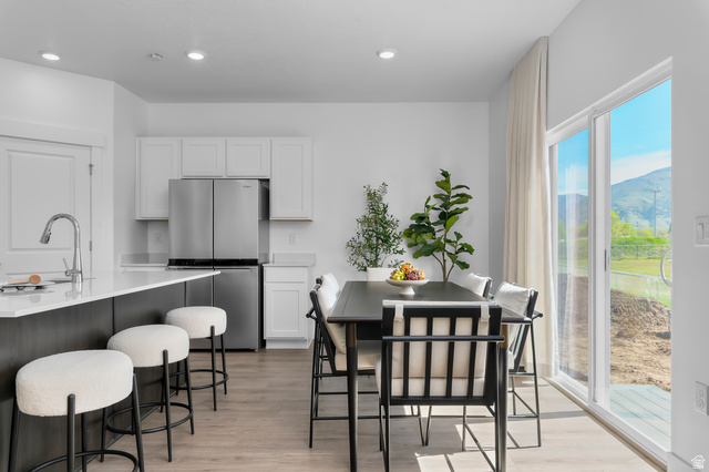 2819 South 710th West, Unit 14 Logan, UT 84321 - Photo 12 of 24 Open-concept kitchen and dining area featuring light wood-finish flooring, white cabinetry, a large kitchen island with a stainless steel sink, and a sliding glass door leading to the exterior