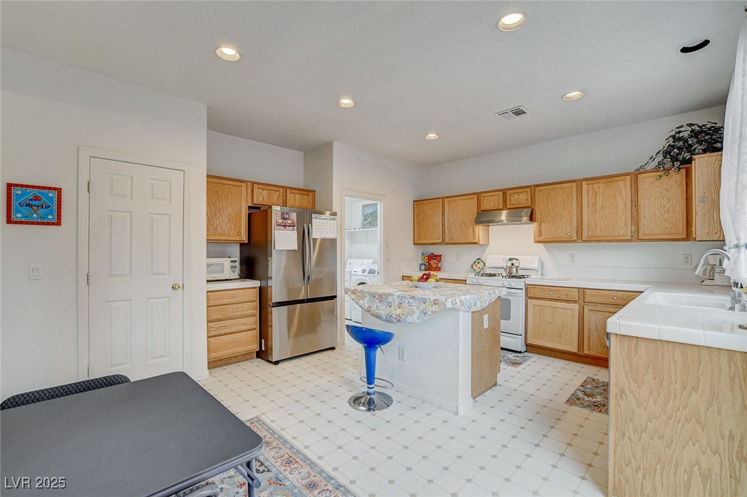 7427 Wagonwheel Ranch Way Las Vegas, NV 89113 - Photo 13 of 50 Kitchen with white appliances, under cabinet range hood, washer / clothes dryer, light countertops, and a kitchen island