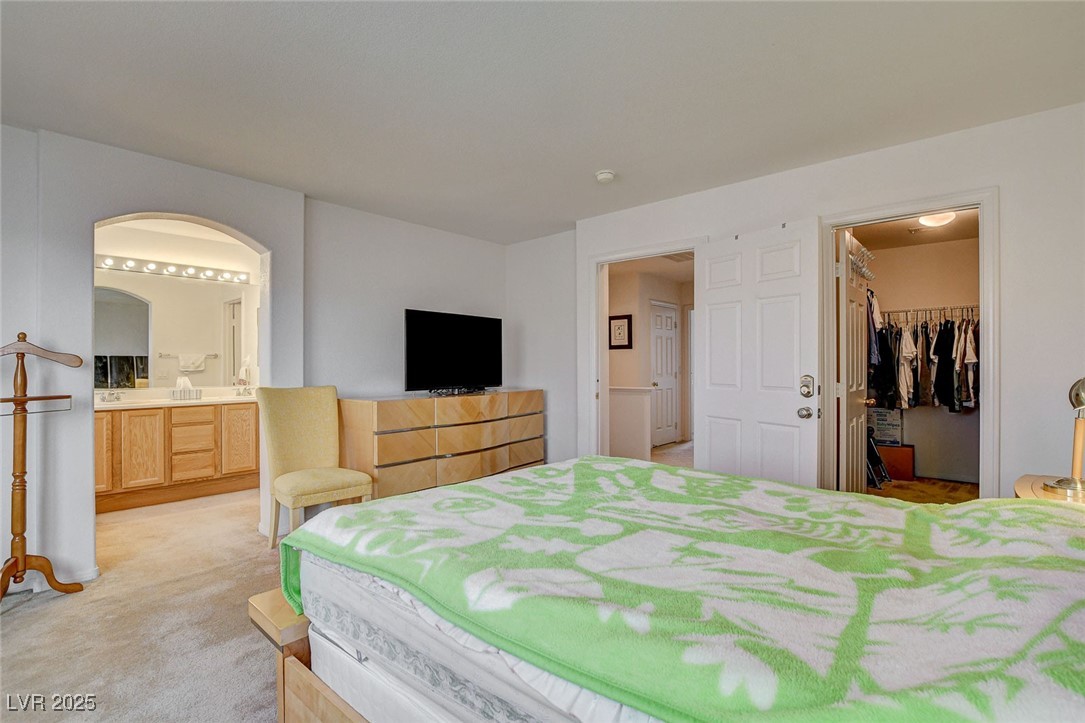 7427 Wagonwheel Ranch Way Las Vegas, NV 89113 - Photo 32 of 50 Bedroom featuring light carpet, arched walkways, a walk in closet, connected bathroom, and a closet