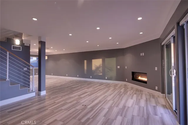 a view of an empty room with wooden floor staircase and a kitchen