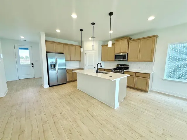 a kitchen with stainless steel appliances a stove a sink a refrigerator white cabinets and wooden floor