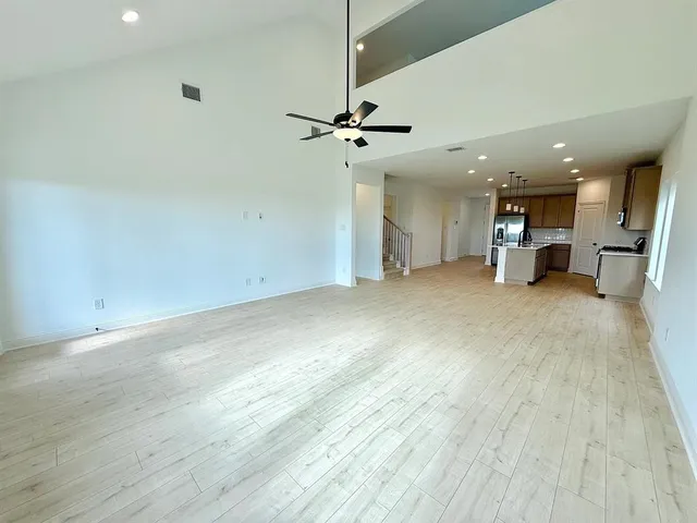 an empty room with wooden floor a ceiling fan and kitchen view