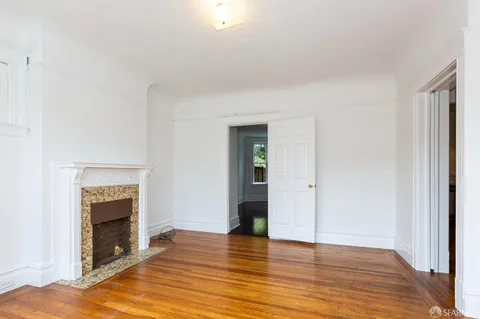 a view of an empty room with wooden floor fireplace and a window