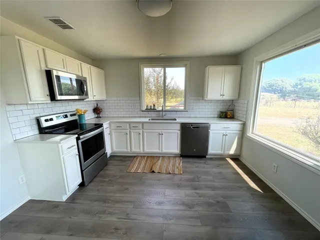 a kitchen with stainless steel appliances granite countertop a stove top oven a sink dishwasher a microwave oven and a refrigerator with wooden floor