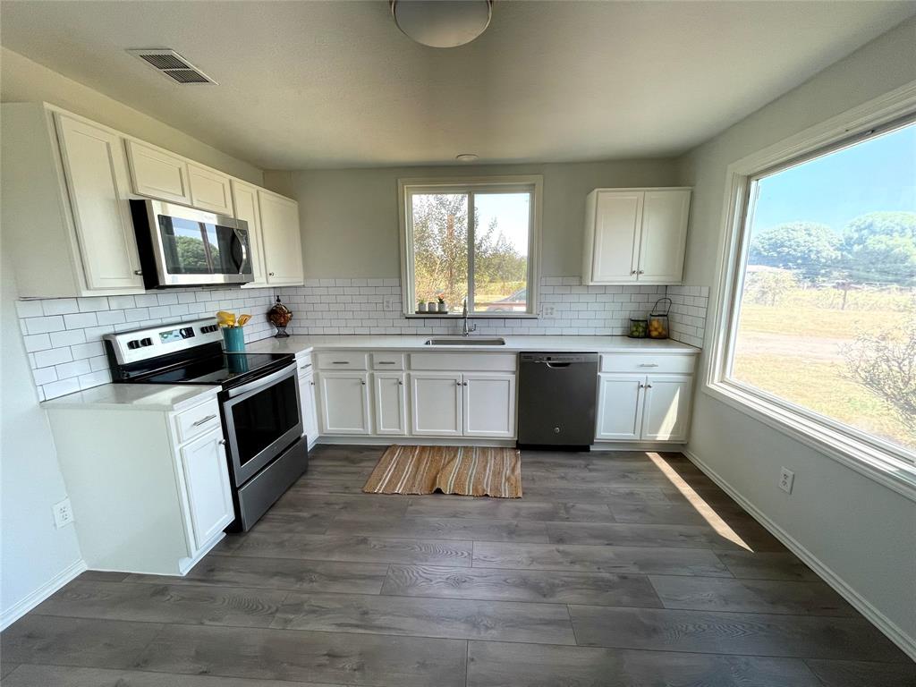 7976 Bearhill Road Royse City, TX 75189 - Photo 3 of 27 a kitchen with stainless steel appliances granite countertop a stove top oven a sink dishwasher a microwave oven and a refrigerator with wooden floor