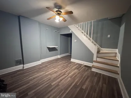 a view of an empty room with wooden floor and a ceiling fan