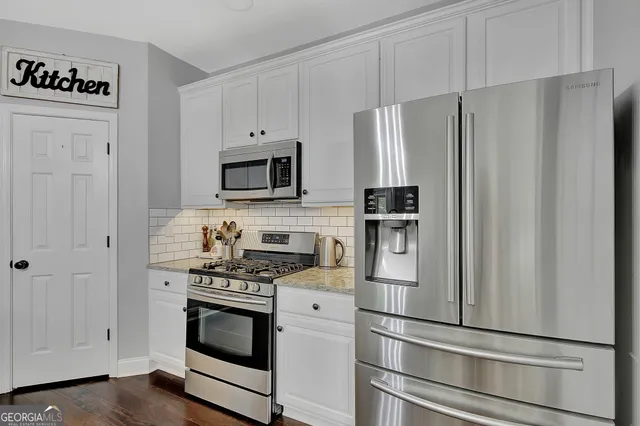 a open kitchen with stainless steel appliances granite countertop a stove top oven a sink a dining table and chairs with wooden floor