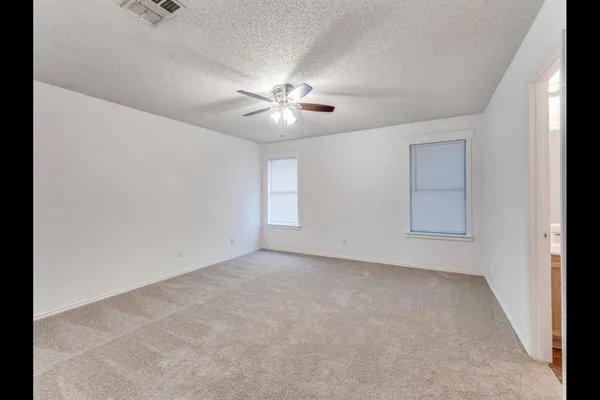 an empty room with chandelier fan and windows