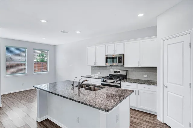 a kitchen with stainless steel appliances granite countertop a sink dishwasher a stove and a refrigerator with wooden floor