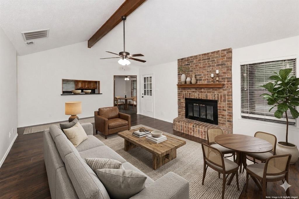 1001 Rosebud Drive Azle, TX 76020 - Photo 8 of 36 Spacious living area featuring a brick fireplace, vaulted ceiling with exposed wood beam, wood-finish flooring, a ceiling fan, and a pass-through window to the kitchen