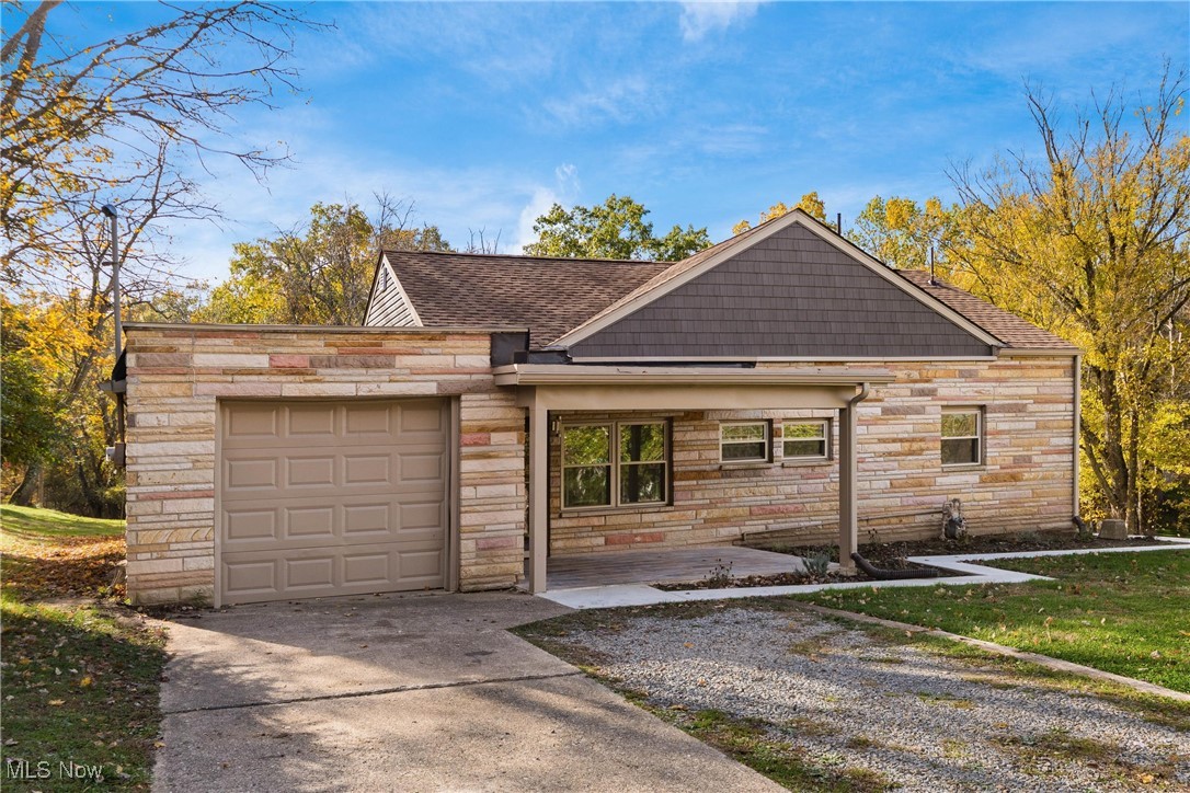 View of front facade featuring stone siding, driveway, a shingled roof, a garage, and a front lawn