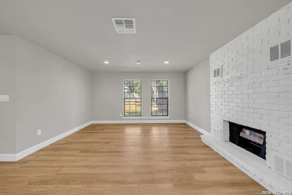 a view of an empty room with wooden floor fireplace and a window