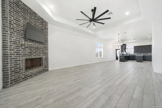a view of a livingroom with a fireplace a ceiling fan and wooden floor