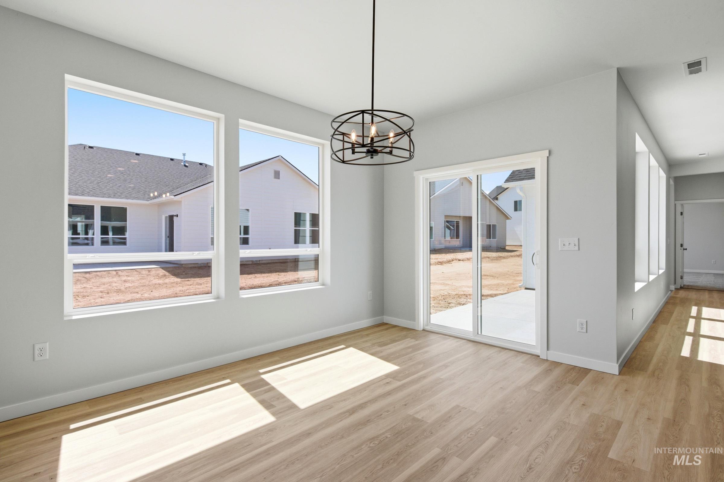 13649 Inman Court Caldwell, ID 83607 - Photo 7 of 22 Bright interior space featuring light wood-finish flooring, a modern black chandelier, large picture windows, a sliding glass door, and light gray wall paint