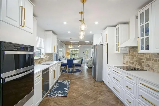a kitchen with stainless steel appliances kitchen island granite countertop a refrigerator oven a sink dishwasher and white cabinets next to a window