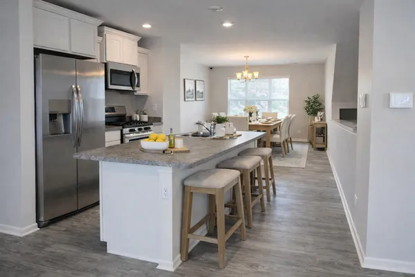 a kitchen with stainless steel appliances granite countertop a dining table chairs refrigerator and sink