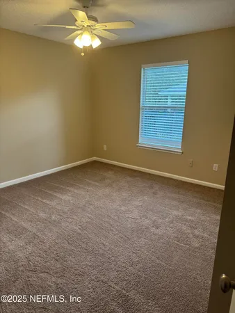 a view of an empty room with window and chandelier fan