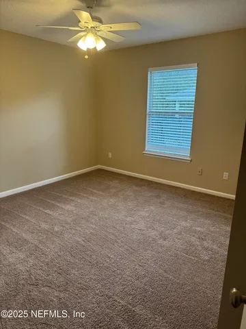 a view of an empty room with window and chandelier fan