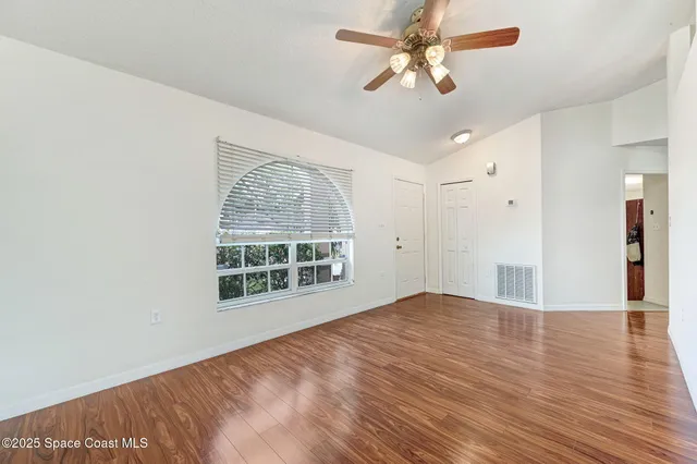 an empty room with wooden floor chandelier fan and windows