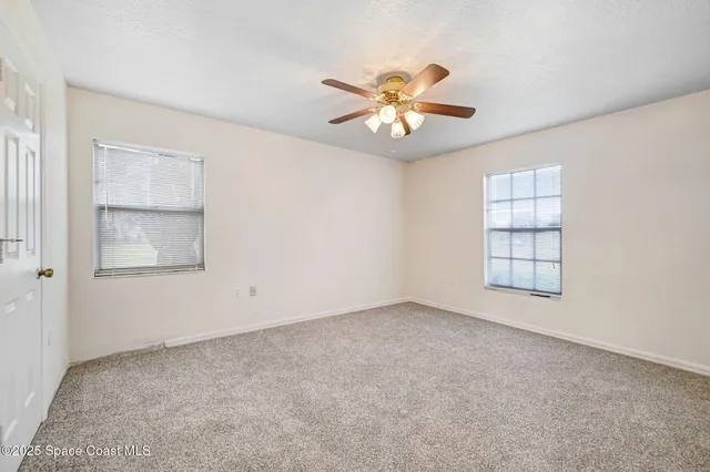 an empty room with windows and chandelier fan