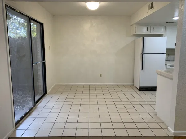 a view of a refrigerator in kitchen and an empty room in wooden floor