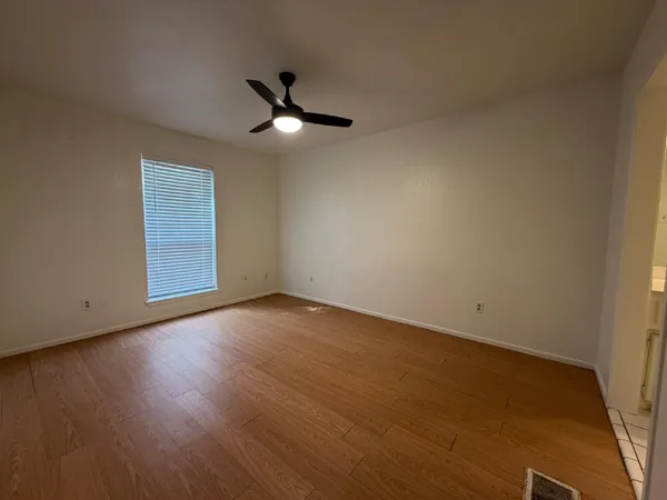 an empty room with wooden floor fan and windows
