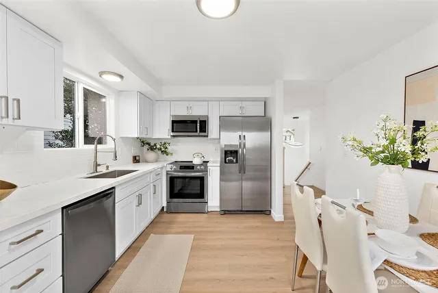 a kitchen with stainless steel appliances granite countertop a sink a stove a refrigerator cabinets and a dining table