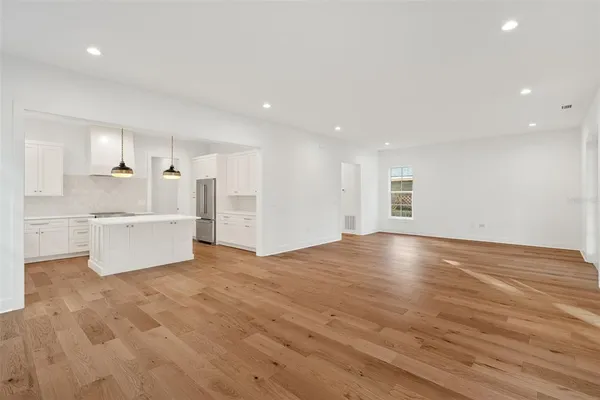 a view of kitchen and empty room with wooden floor