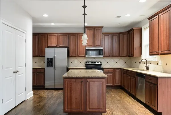 a kitchen with stainless steel appliances granite countertop a refrigerator a sink dishwasher a s stove top oven a refrigerator and white cabinets with wooden floor