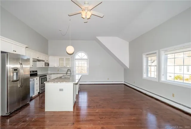 a kitchen with stainless steel appliances granite countertop a stove a refrigerator a sink dishwasher and white cabinets with wooden floor