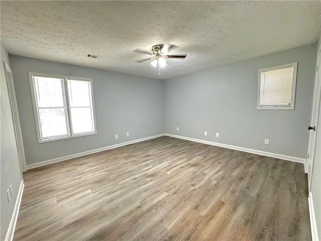 an empty room with wooden floor chandelier fan and windows
