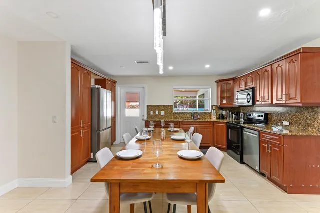 a open dining room with stainless steel appliances kitchen island granite countertop a table chairs and a refrigerator