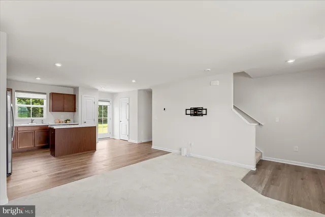 an empty room with wooden floor and kitchen view