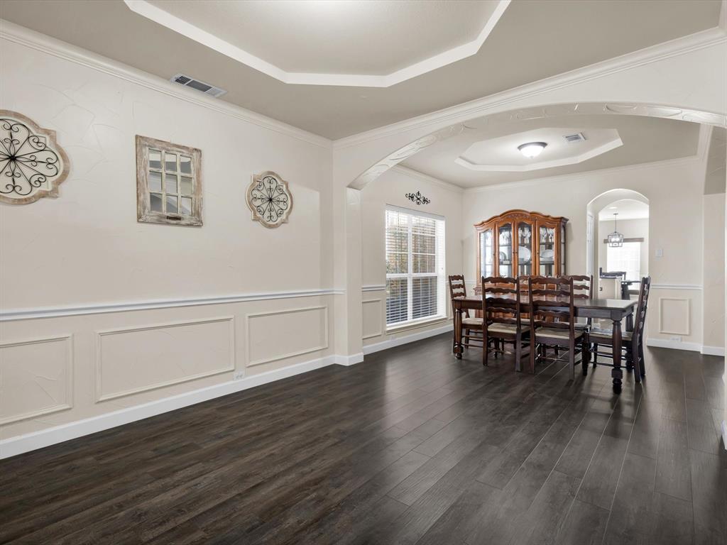 1803 Timber Ridge Drive Frisco, TX 75036 - Photo 11 of 40 Dining area with a raised ceiling, arched walkways, a decorative wall, dark wood-style flooring, and wainscoting