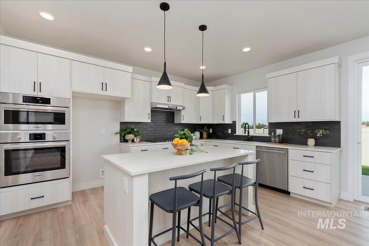 2702 West Gidran Meridian, ID 83642 - Photo 9 of 30 Kitchen featuring a breakfast bar, decorative light fixtures, a kitchen island, stainless steel appliances, and light wood-style floors