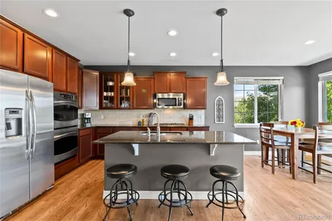 a kitchen with stainless steel appliances granite countertop a stove top oven a refrigerator a sink and chairs