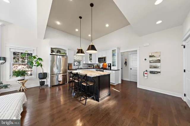 a open kitchen with stainless steel appliances kitchen island granite countertop a refrigerator a stove a sink a dining table and chairs with wooden floor