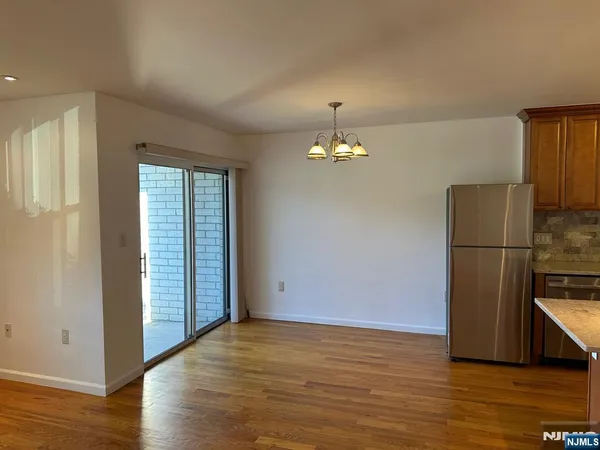 an empty room with wooden floor kitchen view and windows